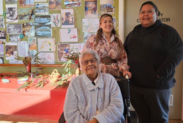 Tarli Dean Atkinson and Ebony Joachim with an Elder in front of the Elders Arts Program display